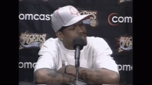 Man in Hat and White Shirt Talking Into Microphone