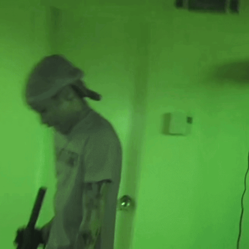 Man In Hat Holding Gun In Green Lit Room GIF