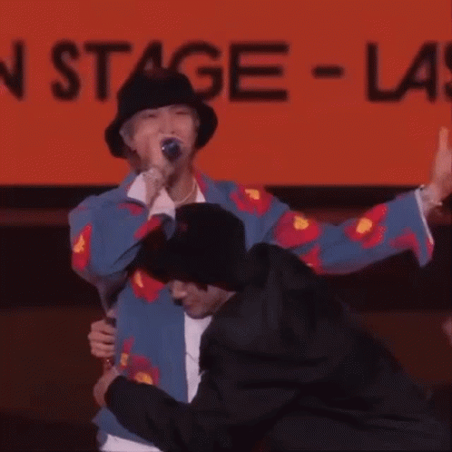 Man in Hat Hugging Man in Front of Stage Sign