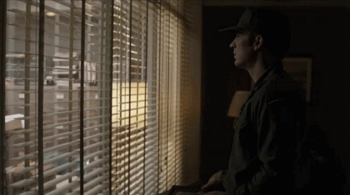 Man in Hat Looking Out Window With Blinds