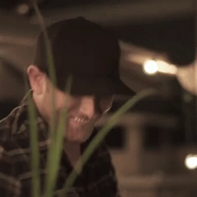 Man in Hat Smiling and Thumbs Up Next to Plant