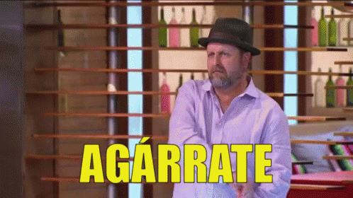 Man in Hat Standing Before Agárrate Sign