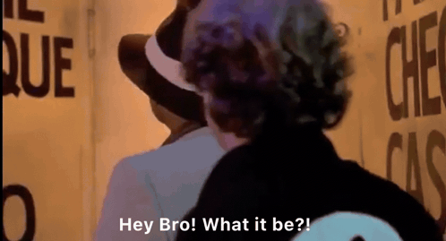 Man in Hat Talking to Man at Sign Hey Bro What It Be