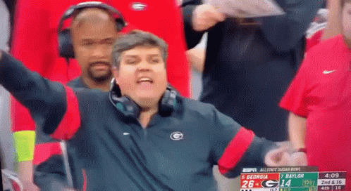 Man in Headphones and Jacket with Letter G Watching Football