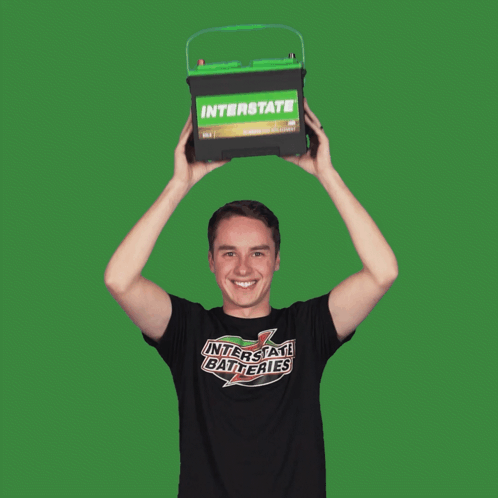 Man in Interstate Batteries Shirt Holding Green Battery Over Head