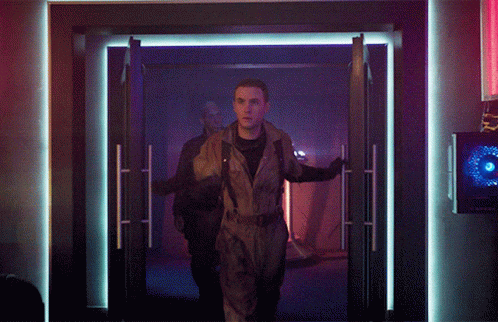 Man In Jumpsuit Walking Through Doorway In Dark Room GIF