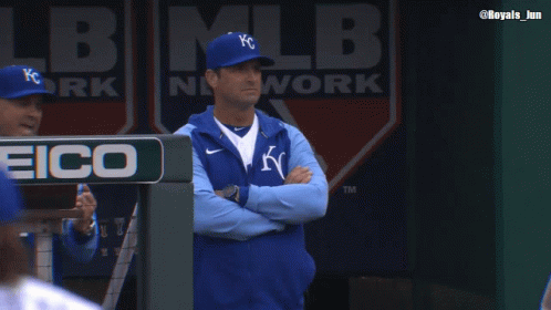 Man in KC Hat Stands in Dugout With Arms Crossed
