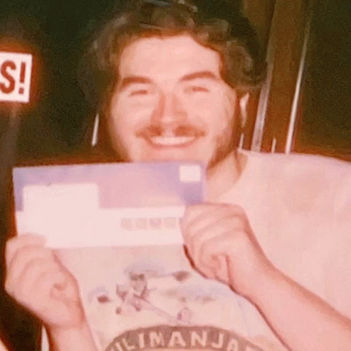 Man in Kilimanjaro Shirt Smiling Holding Purple Envelope