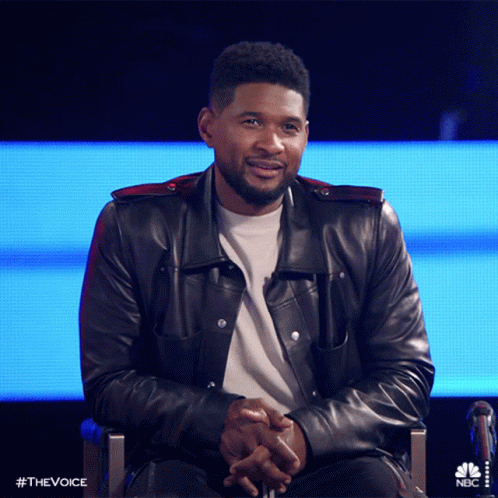 Man in Leather Jacket Sitting With Hands Folded in Front of NBC Screen