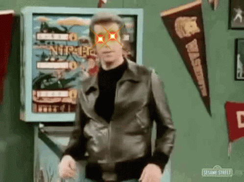 Man in Leather Jacket Standing in Front of Pinball Machine With Red Eye