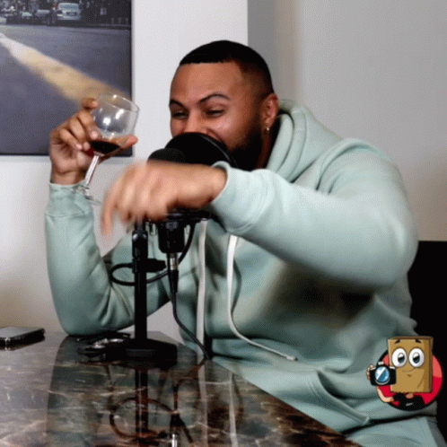 Man In Light Blue Sweatshirt Holding Wine Glass At Microphone GIF