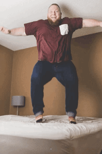Man in Maroon Shirt Jumping on Bed