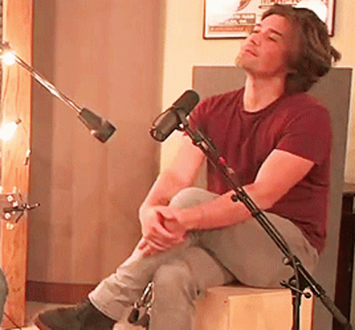 Man in Maroon Shirt Sitting on Box by Microphone