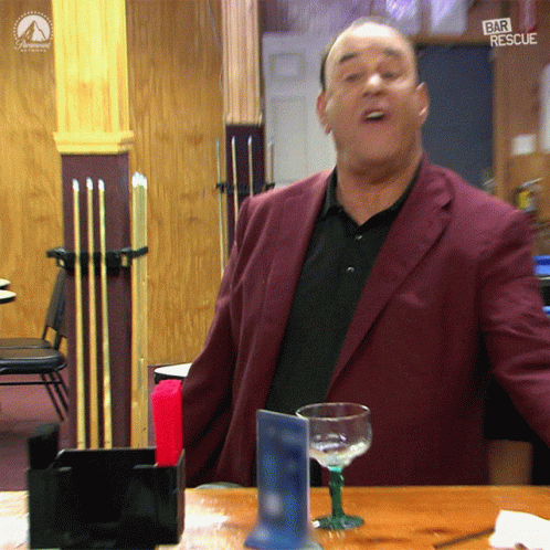 Man in Maroon Suit Standing in Front of Bar Rescue Sign