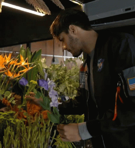 Man In NASA Jacket Looking At Purple Flowers GIF