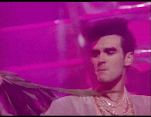 Man in Necklace and Wig Dancing on Pink Background