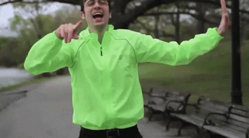 Man in Neon Green Jacket With Arms Outstretched in Park