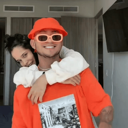 Man in Orange Hat and Sunglasses Carrying Woman on Back