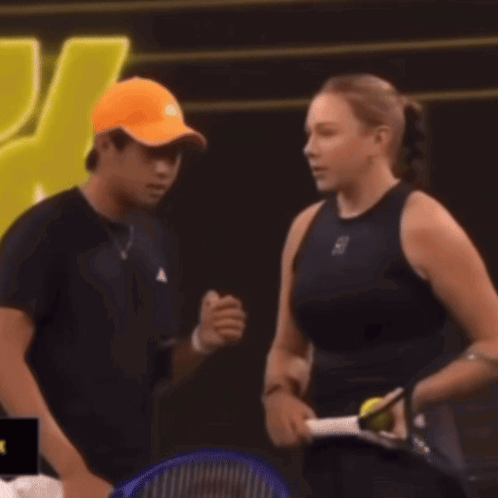 Man in Orange Hat Talking to Woman With Tennis Racquet