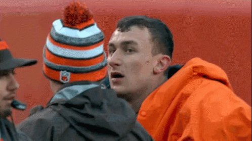 Man in Orange Jacket and Hat Talking to Another Man