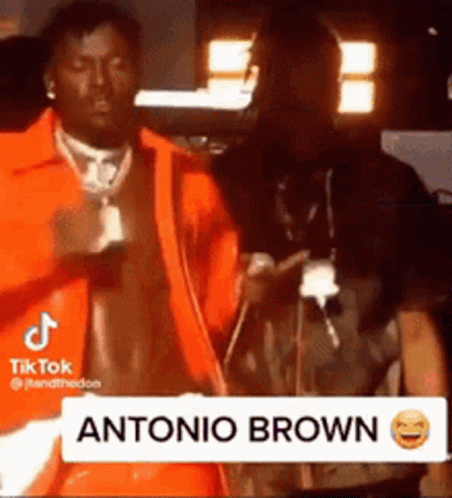 Man in Orange Jacket Next to Man in Dark Room