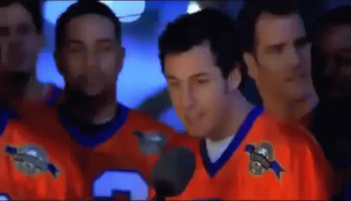 Man in Orange Jersey Talking Into Microphone With Men