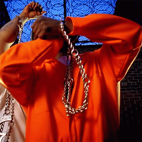Man in Orange Jumpsuit Chained to Fence