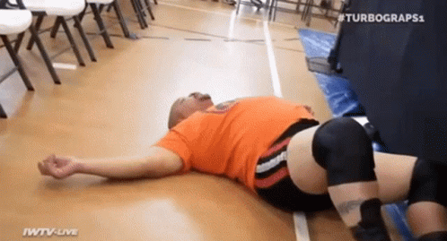 Man In Orange Shirt Lying In Wrestling Ring GIF
