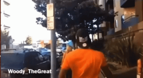 Man In Orange Shirt Walking Down Street Woody The Great GIF