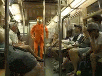Man In Orange Suit Standing In Train GIF