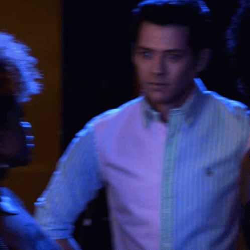 Man In Pink And Blue Striped Shirt In Dark Room GIF