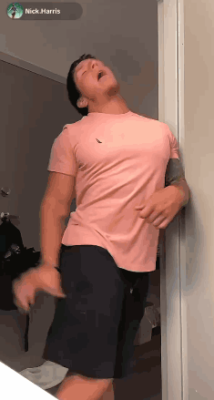 Man In Pink Shirt And Black Shorts Leaning Against Wall GIF