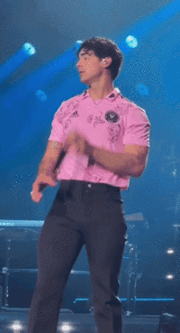 Man In Pink Shirt Singing Into Microphone On Stage GIF