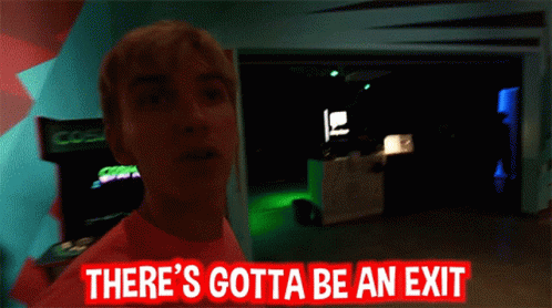 Man in Pink Shirt Standing in Dark Room With Sign Somewhere Over Here