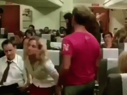 Man in Pink Shirt Standing in Front of Group on Airplane