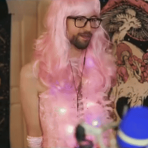 Man in Pink Wig and Glasses by Skull Wall