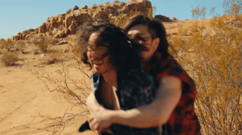 Man In Plaid Shirt Carrying Woman In Desert GIF