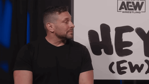 Man in Plaid Shirt in Front of Hey Crew Sign
