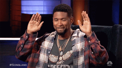 Man In Plaid Shirt Sitting In Chair With Hands Up And NBC Logo GIF