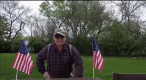 Man In Plaid Shirt With Two Small American Flags GIF
