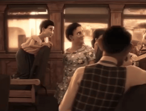 Man In Plaid Vest Next To Woman In Dress GIF