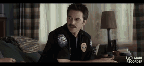Man In Police Uniform With Mustache Sitting On Couch In Bedroom GIF