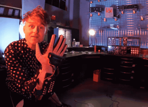 Man in Polka Dot Shirt Holding Gloves and Remote
