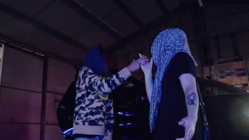 Man in Purple Scarf High-Fives Another in Dark Room