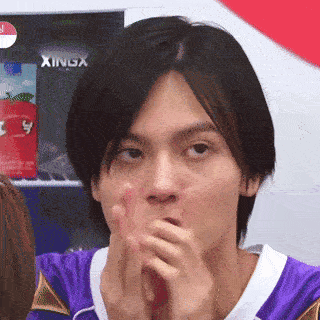 Man in Purple Shirt Covering Mouth with Xingx Sign
