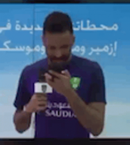 Man in Purple Shirt Holding Phone in Front of TV