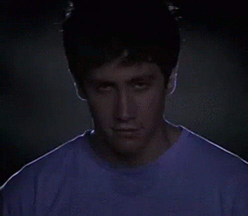 Man in Purple Shirt Looking at Camera in Dark