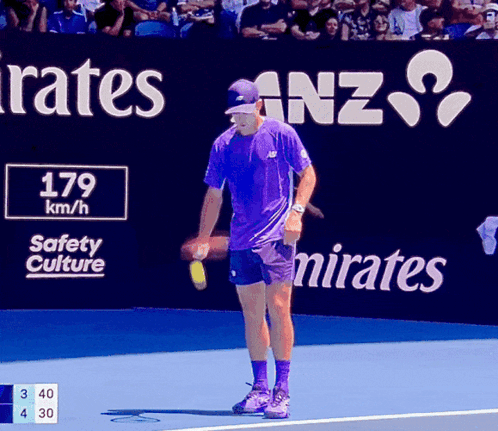 Man in Purple Shirt on Tennis Court in Front of Emirates Sign