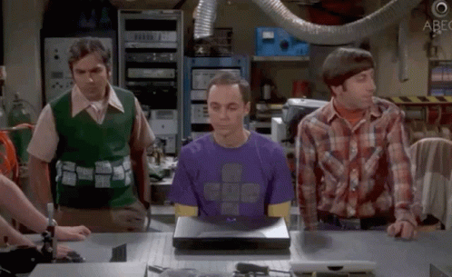 Man in Purple Shirt Sitting at Laptop With Two Men Looking On
