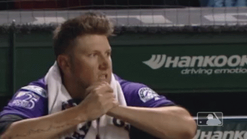 Man in Purple Shirt Sitting in Dugout With Hankook Ad